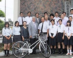 石巻市立女子高等学校の前で三国校長（中央右）と生徒の皆さんと。ベイリー社長（前列中央左）、会長の柳瀬房子（左隣）、特別顧問の吹浦忠正（後列中央左）