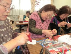 だるま人形を制作する二宮さん（左）と石巻市北上仮設の皆さま（宮城県東松島市内響仮設住宅、2012年3月8日）