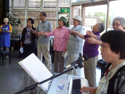 参加者に祝福されながら、照れくさそうに「ここに幸あれ」を歌う坂本さん夫妻（左から4～5人目）＝花巻市西宮野目の結海で