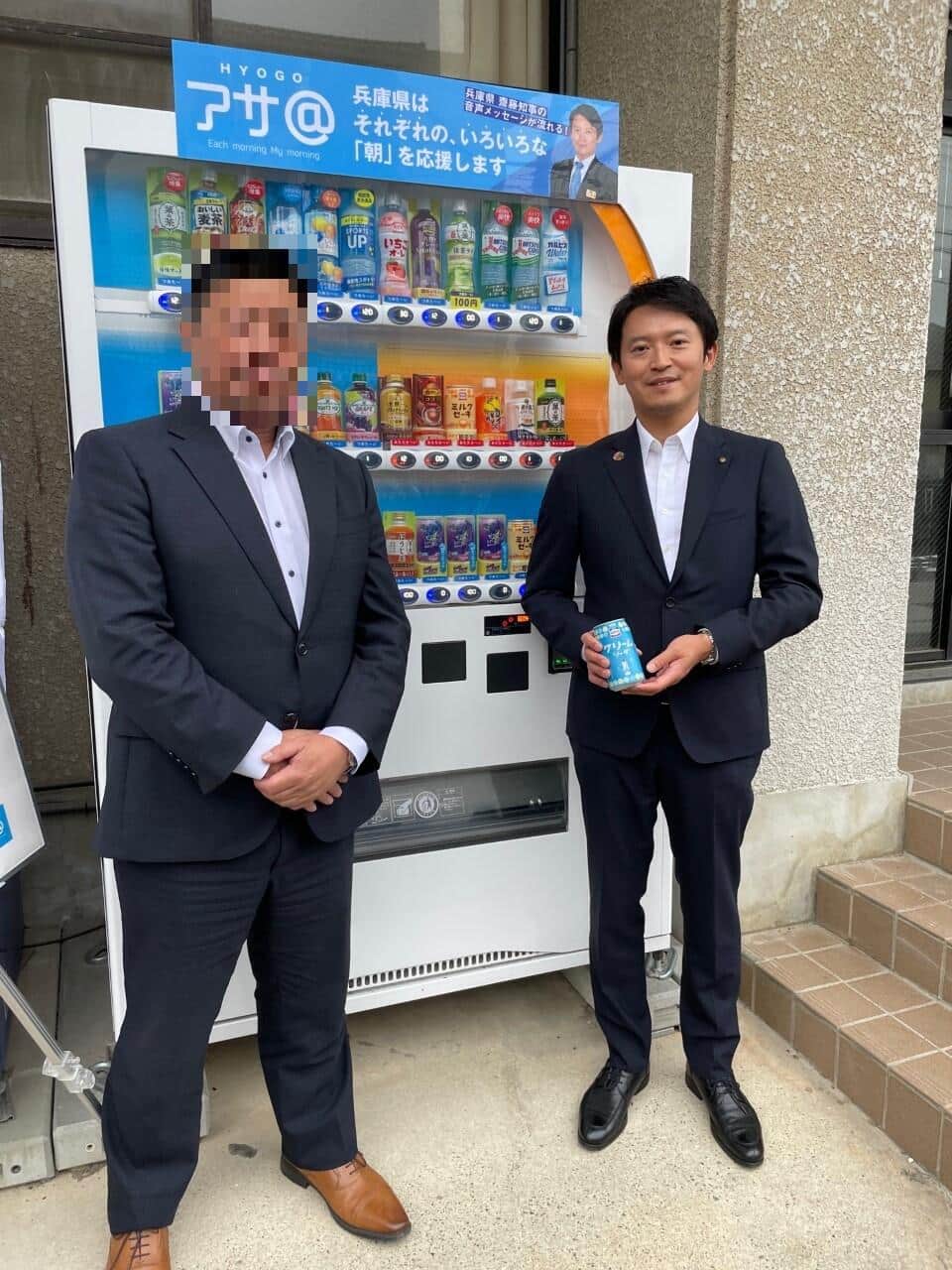 自販機とジュースを持つ斎藤氏（飲料メーカーのプレスリリースから、編集部で一部加工）