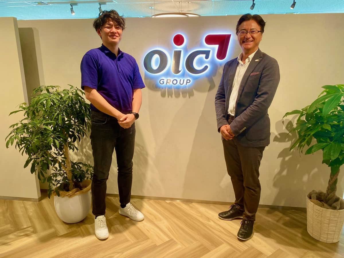 浜野仁志さん、前川孝雄（左から）。ロピアを基幹事業とするOIC グループの会社ロゴ前にて