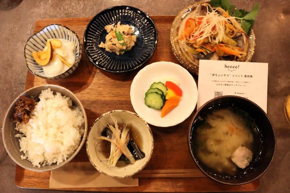 （写真右上から反時計回りに）「鯵の南蛮漬け」「卯の花」「ふぞろいキウイチップスのせヨーグルトのデザート」「昆布と鰹節のおかかのっけご飯」「なすの煮浸し」「お味噌汁」（中央の白い皿は、ぬか漬け）